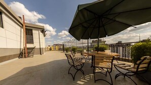 A rooftop terrace with outdoor seating, a large umbrella, and a view of surrounding buildings. - Cozy,all-equipped 1-bedroom apartment with cafe,gym &minimart in Uptown Nairobi. (Nairobi)