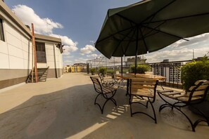 A rooftop terrace with outdoor seating, a large umbrella, and a view of surrounding buildings. - Cozy,all-equipped 1-bedroom apartment with cafe,gym &minimart in Uptown Nairobi. (Nairobi)