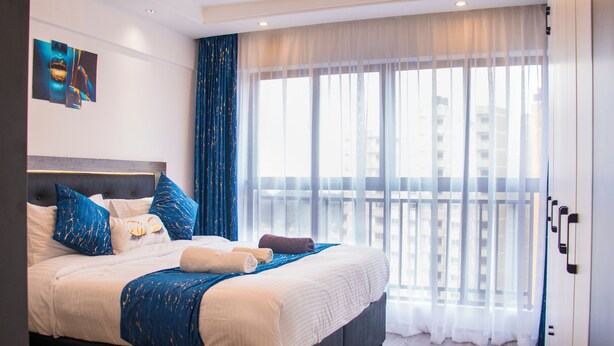 A modern hotel room with a large bed, a view of the city, and a balcony. - Cozy,all-equipped 1-bedroom apartment with cafe,gym &minimart in Uptown Nairobi. (Nairobi)