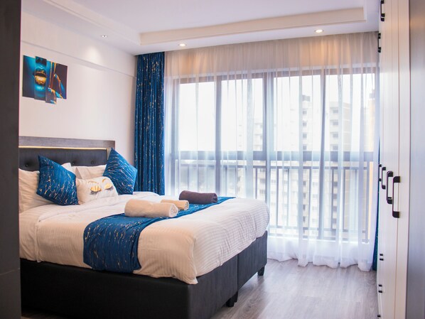 A modern hotel room with a large bed, a view of the city, and a balcony. - Cozy,all-equipped 1-bedroom apartment with cafe,gym &minimart in Uptown Nairobi. (Nairobi)