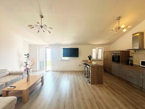 A spacious living area with a wooden floor, a sofa, a coffee table, a TV mounted on the wall, a kitchen with modern appliances, and a ceiling fan. - Vacation apartment with beautiful sea view and pool (Crikvenica)