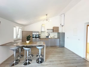 A modern kitchen with a central island, bar stools, a built-in oven, microwave, and a refrigerator. - Vacation apartment with beautiful sea view and pool (Crikvenica)
