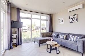 Una sala de estar moderna con un sofá gris, una mesa de centro redonda de madera y un gran ventanal con cortinas.