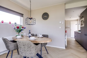 A dining area with a round table, chairs, a vase with flowers, a bottle, and glasses.