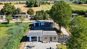 A modern residential area with multiple houses, a large open field, and a body of water in the background. - Cube XL 68 | 4 persoons chalet in Zennewijnen (Zennewijnen)