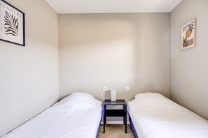 Een kamer met twee eenpersoonsbedden, een tafeltje met een lamp, en twee lichtschakelaars aan de muur.