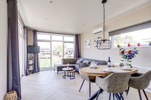 Een moderne eetruimte met een ronde tafel, grijze bekleden stoelen en uitzicht op het buitengebied.