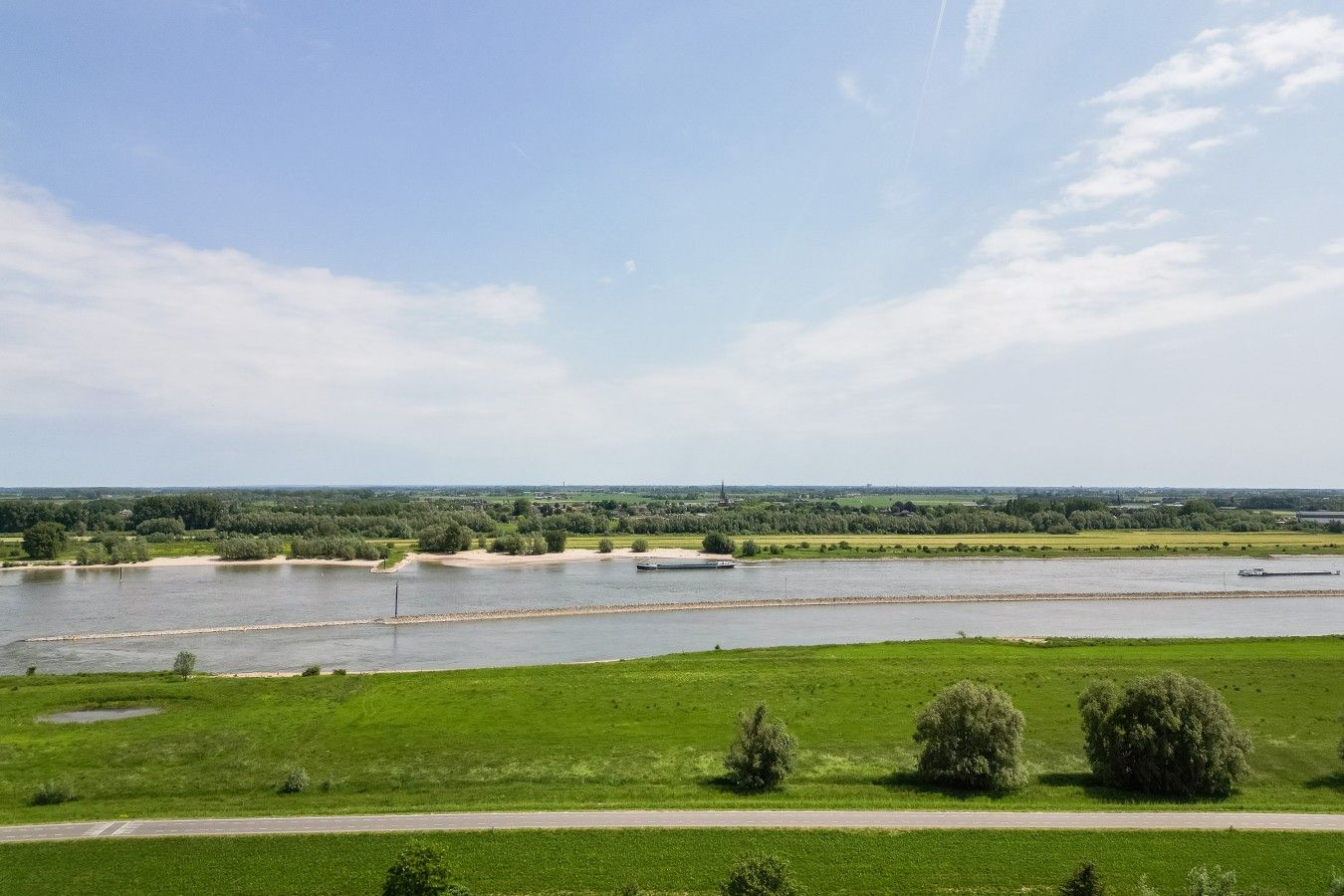 Ein Fluss mit einer Brücke, grünen Feldern und blauem Himmel.