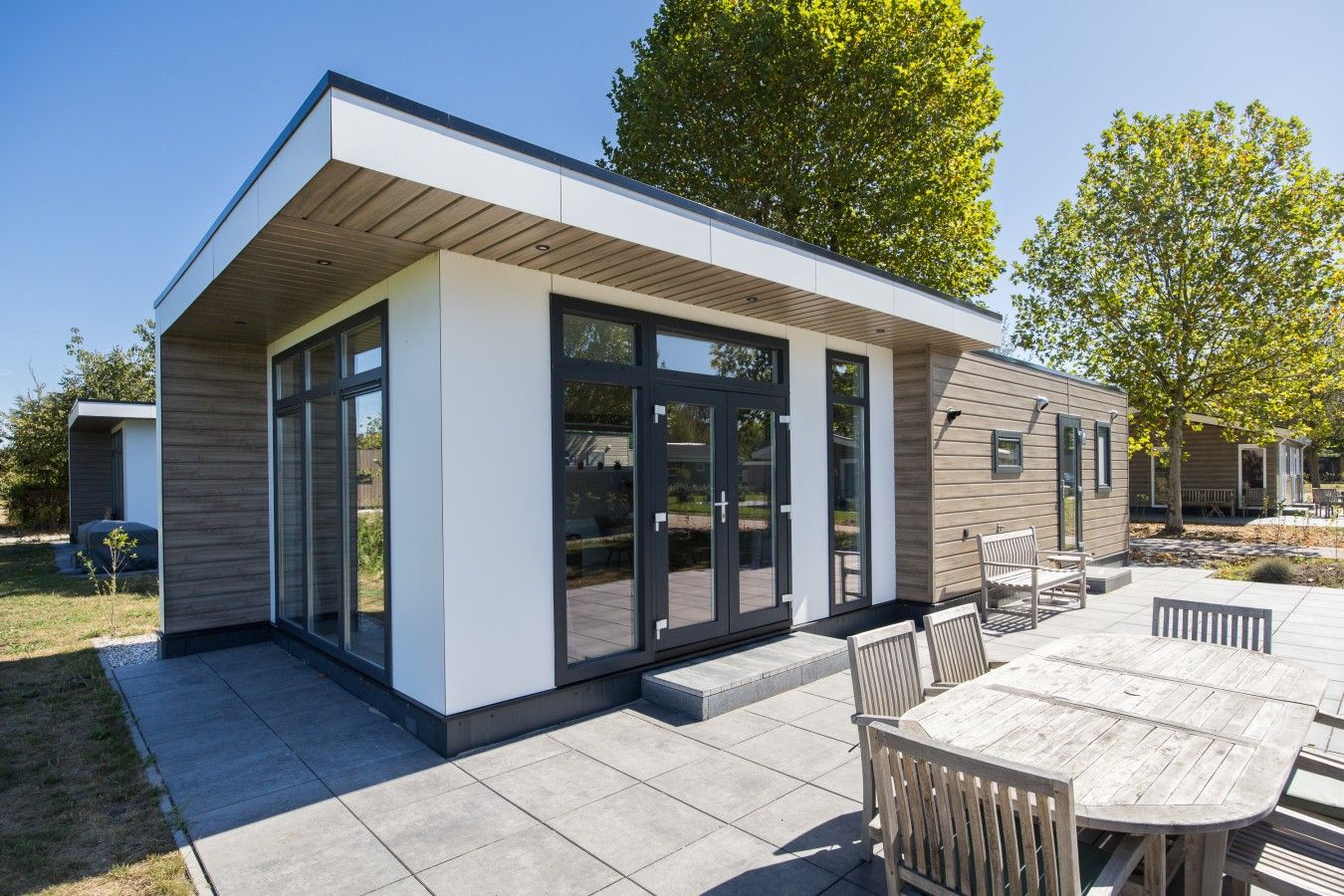 Een modern huis met een patio, grote schuiframen en een houten terras.