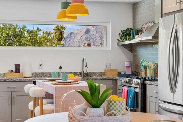 A modern kitchen with a view of mountains, a stainless steel refrigerator, and a dining area with a table and chairs. - Whimsical Palm Springs Retreat - A Ryson Property (Palm Springs)