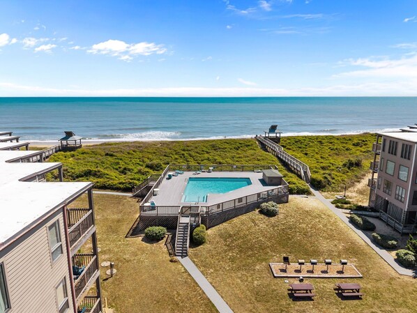 Ein Poolbereich mit Blick aufs Meer, umgeben von Gebäuden und einer Rasenfläche.