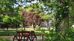 A wooden bridge over a stream in a park with trees and a building in the background. - 2-person Bell Tent Stay at Old Vicarage Campsite (Retford)