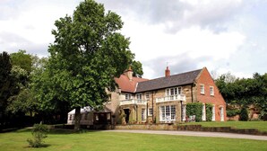 A large stone building with a prominent tree in front, a paved driveway, and a small garden area. - 2-person Bell Tent Stay at Old Vicarage Campsite (Retford)