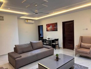 A modern living room with a sofa, a coffee table, a dining area with chairs, and a painting on the wall.