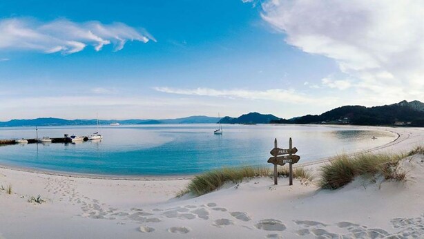 A beach with a signpost, a boat, and a distant ship.