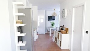 A hallway with a white shelving unit, a dining area with a table and chairs, a clock on the wall, and a door on the right.