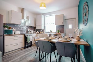 A modern kitchen with a dining area, featuring a stove, microwave, cabinets, and a dining table set for four. - Golden Aqua Haven Retreat | Free Parking | 14PPL (Sheffield)