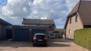 A paved driveway leading to a garage, a parked car, and a building with a tiled roof. - Last-minute for the trade fair: 4-room apartment just 7 minutes away! (Laatzen)