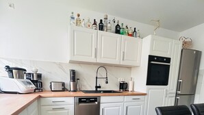 A modern kitchen with white cabinets, a stainless steel dishwasher, a coffee maker, and a variety of bottles on the countertop. - Last-minute for the trade fair: 4-room apartment just 7 minutes away! (Laatzen)