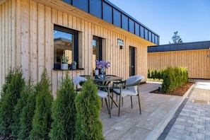 A modern building with wooden exterior walls, a patio with a table and chairs, and potted plants. - Tiny Home “Auerberg Sweet” with Private Terrace and Wi-Fi (Stötten am Auerberg)