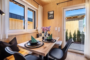 A dining area with a wooden table, black chairs, and a view of the outdoors through a sliding glass door. - Tiny Home “Auerberg Sweet” with Private Terrace and Wi-Fi (Stötten am Auerberg)