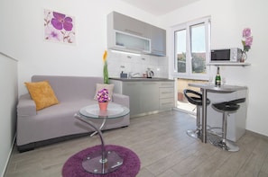 A compact living space with a kitchenette, a sofa with a cushion, a small round table with a vase, and a purple rug. - Studio Talir with terrace (Dubrovnik)