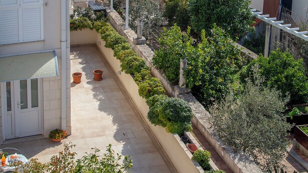 Een balkon met potplanten, uitzicht op zee en gebouwen met terracotta daken.