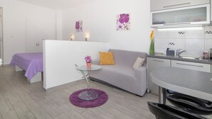 Een moderne kamer met een bank, een klein rond tafeltje, een glazen scheidingswand, een kitchenette en kunstwerken aan de muur.
