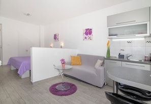A modern room with a sofa, a small round table, a glass partition, a kitchenette, and artwork on the walls. - Studio Talir with terrace (Dubrovnik)