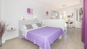 Een slaapkamer met een bed, nachtkastje, klein plankje en een raam.