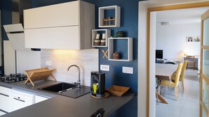 Een moderne keuken met een spoelbak, fornuis en koffiezetapparaat. Er staan planken met decoratieve objecten en er is een eethoek met stoelen.