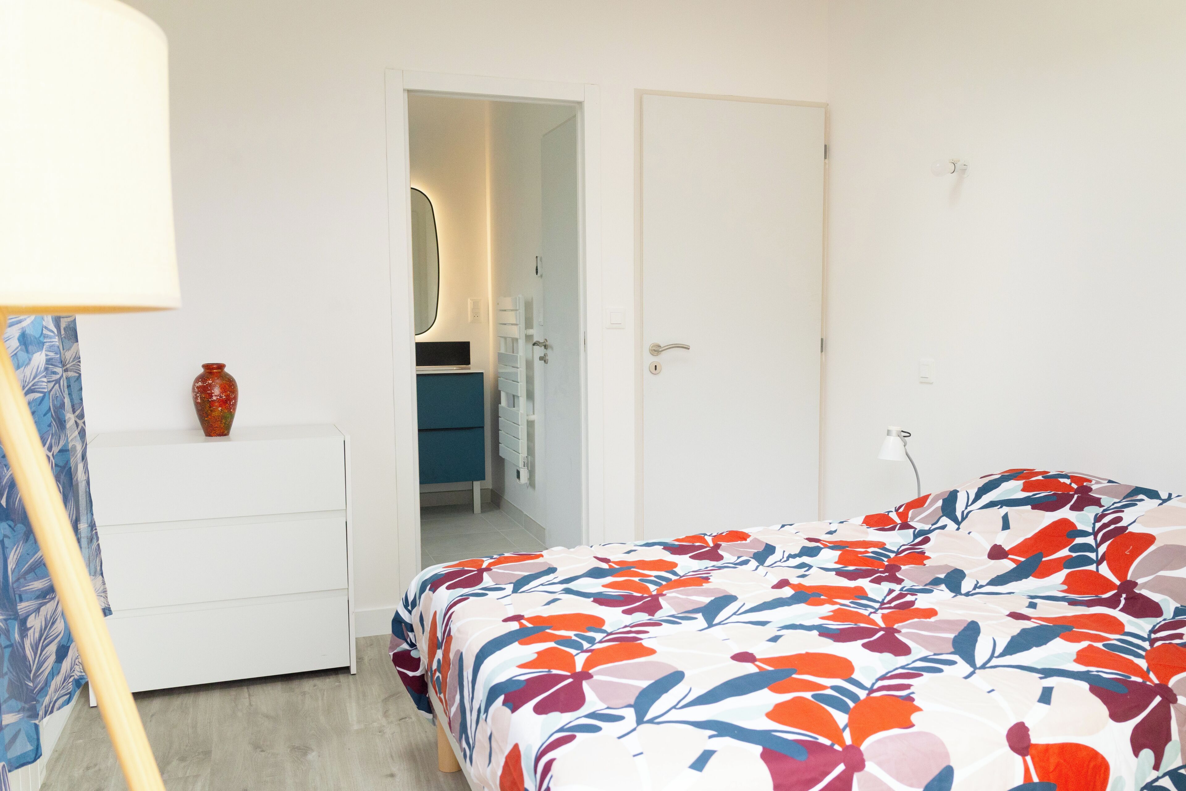 A bedroom with a bed, a dresser, a mirror, and a door leading to a bathroom.