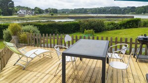 Een houten terras met een tafel, stoelen, een barbecue en uitzicht op een rivier en huizen in de verte.