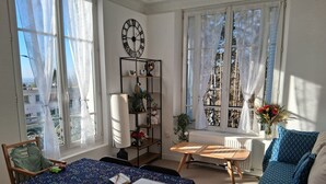 Une pièce chaleureuse avec une table, des chaises, un canapé, une bibliothèque et une grande fenêtre avec des rideaux.