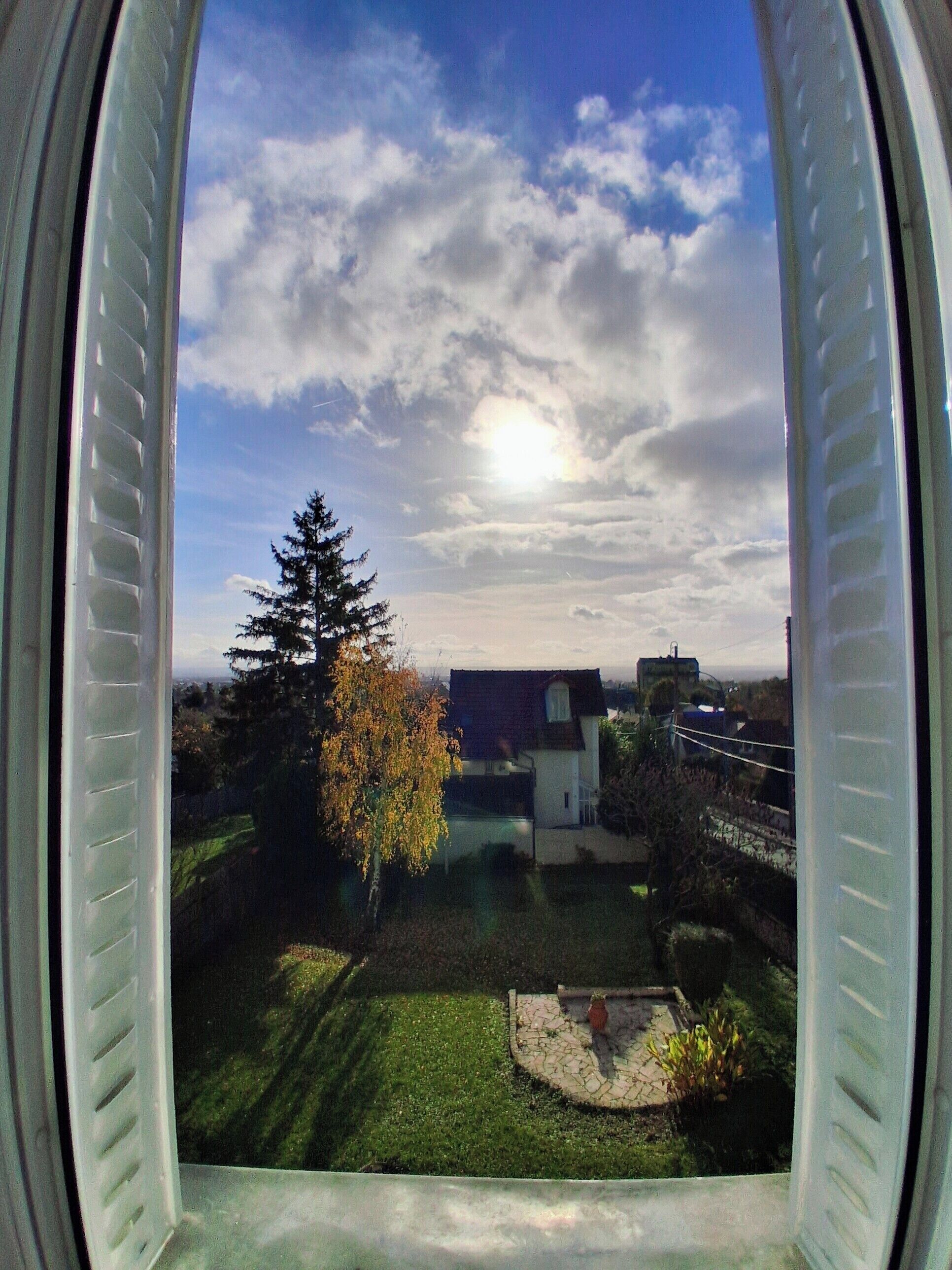 A view through a window with a clear sky, a tree, and a building in the background.