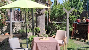 Un espace extérieur aménagé avec une table et des chaises, un parasol vert et un arbre.