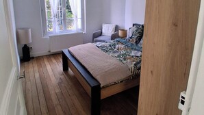 Une chambre avec un plancher en bois, un lit recouvert d’une couvre-lit à motifs, une fenêtre avec des rideaux et un luminaire au plafond.