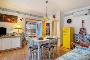 Un coin repas comprenant une table, des chaises, une lampe, un réfrigérateur jaune et un lit recouvert d’une couvre-lit à motifs.
