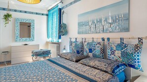 A bedroom with a patterned bedspread, a large painting of sailboats, a hanging lamp, and a decorative mirror. - Apartment 'La Maison Des Artistes' with Wi-Fi and Air Conditioning (Mozzecane)