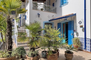 Une cour avec des plantes en pot, une porte bleue et un sol carrelé.