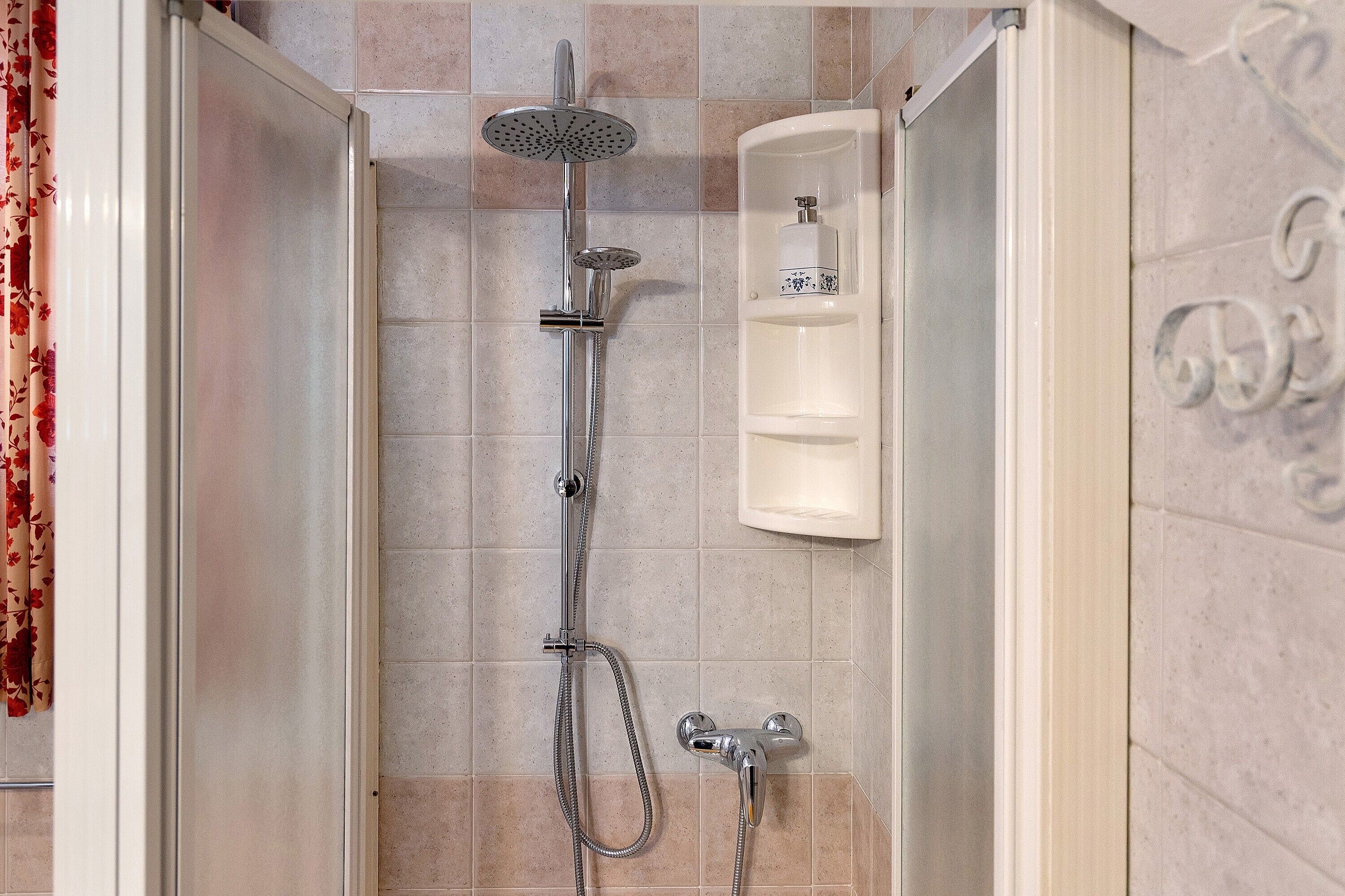 A shower with a handheld showerhead, a handheld showerhead, and a wall-mounted faucet.