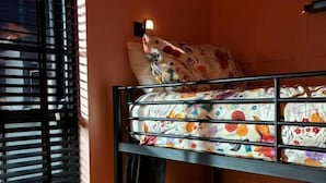 Una litera con ropa de cama floral, una ventana con persianas y un estante fijado a la pared.