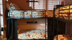 Una habitación con literas, un piso a cuadros, una mesita con una lámpara y un estante en la pared.