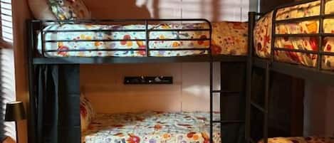 A bunk bed room with a checkered floor, a small table with a lamp, and a wall-mounted shelf.