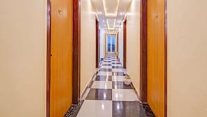 A hotel hallway with checkered flooring, wooden doors, and recessed lighting. - OnlyStay Snap Hotel (Noida)