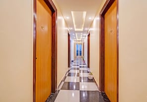 A hotel hallway with checkered flooring, wooden doors, and recessed lighting. - OnlyStay Snap Hotel (Noida)