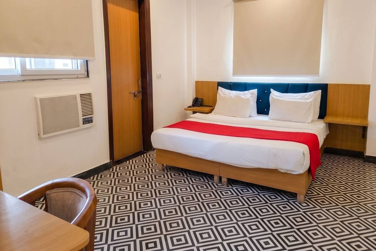 Habitación de hotel con cama, mesita de noche, silla, ventana y aire acondicionado.