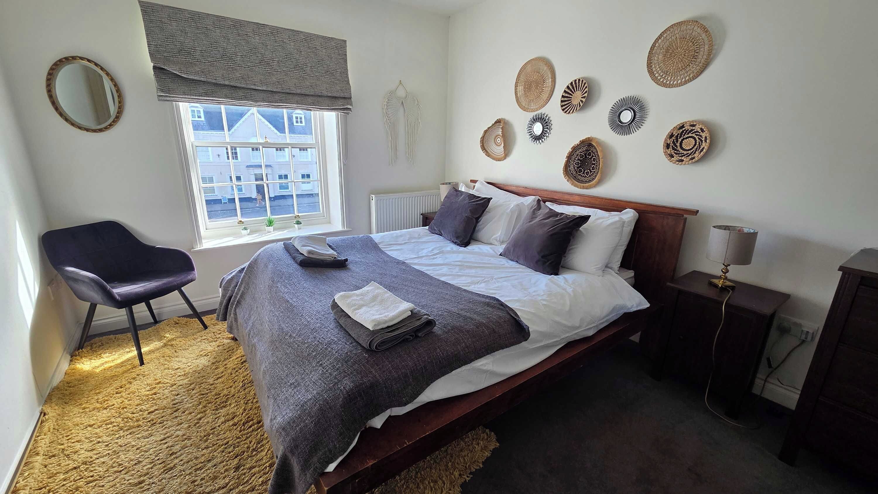 A bedroom with a bed, a chair, a window, and decorative wall art.
