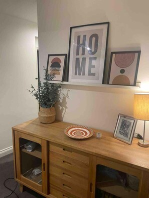 A wooden cabinet with a plant, a framed picture, and a lamp. - Large town centre apartment with parking (Oxfordshire)
