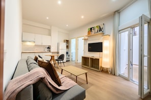 Ein modernes Wohnzimmer mit einer Couch, einem Couchtisch, einem Fernseher und einer Glastür, die auf einen Balkon führt.
